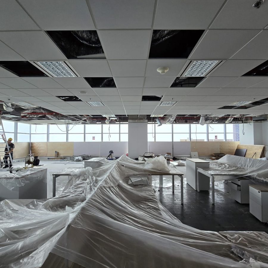 Open office space with workers installing ceiling grids and protective covers on furniture, illustrating an organized reinstatement process