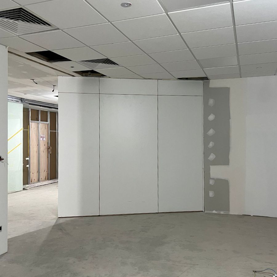 A workspace undergoing transformation with new partition walls being installed, demonstrating precise construction techniques