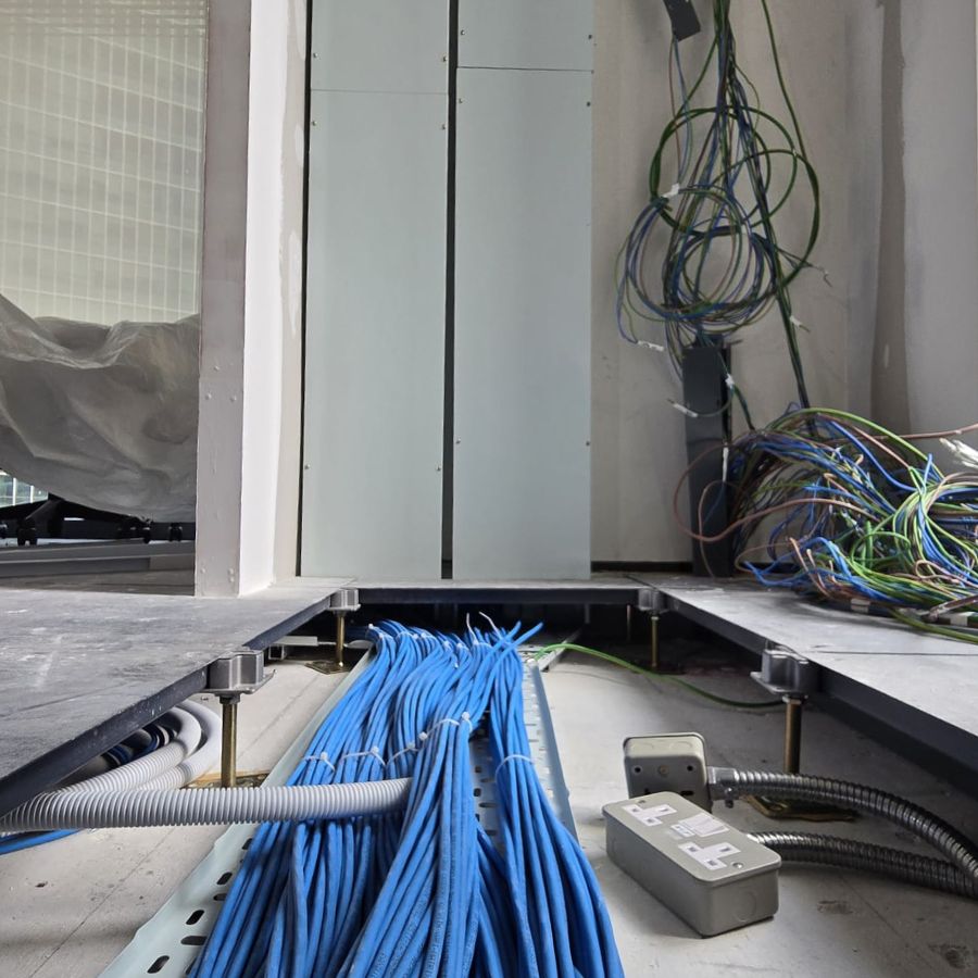 Close-up of raised flooring installation with neatly organized cables and power outlets, showcasing meticulous cable management