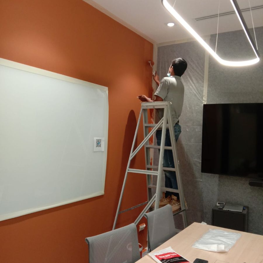 orker on a ladder carefully painting an orange office wall, focusing on clean and professional interior finishing.